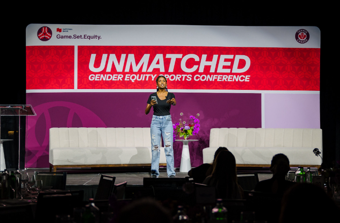 A woman stands on a stage in front of a screen that says "Unmatched: Gender equity sports conference."