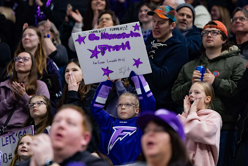 Young PWHL fan holds sign cheering on the Minnesota Frost at a PWHL game.