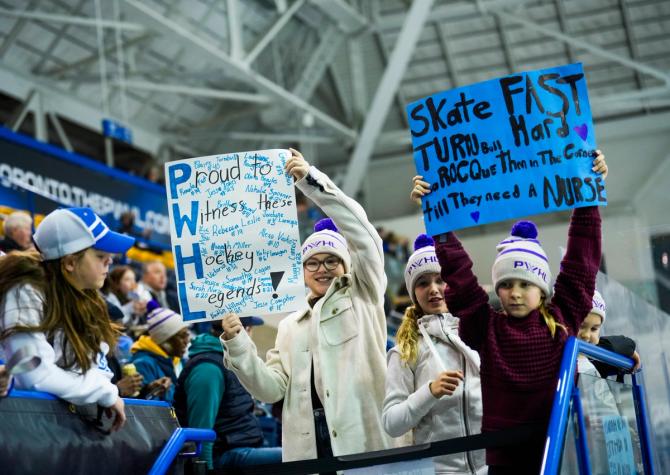 Young PWHL fans holding up posters during a game