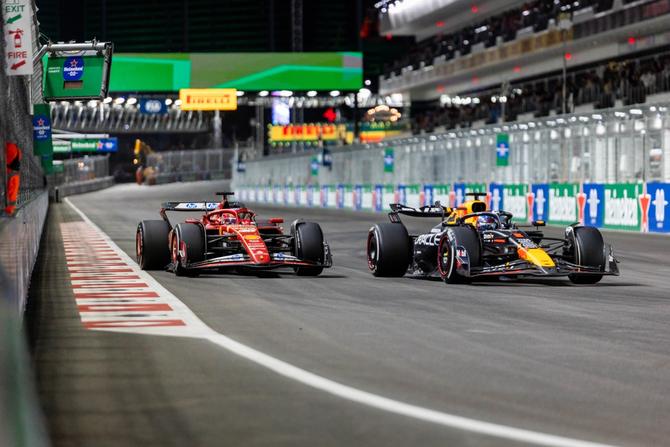 Two Formula 1 cars, a red Ferrari and a dark blue Oracle Red Bull Racing car, racing side by side on a floodlit street circuit at night