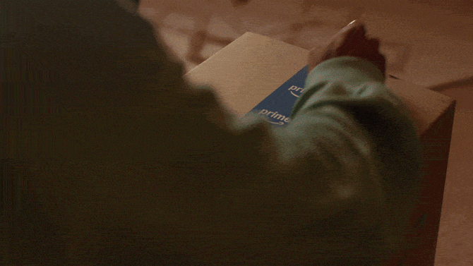 A woman in her living room opens an Amazon box containing an LED face mask, text reads "Me Time. Same Day Delivery. It's on Prime"