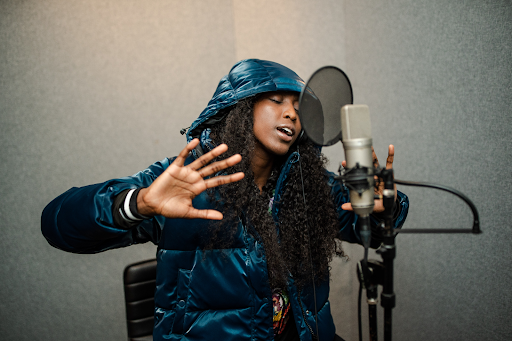 Rapper and college basketball player Flau’jae Johnson sits in front of a microphone in a recording booth.