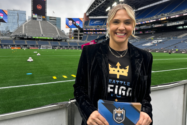 Carla Marie Monica stands in front of a soccer field wearing a velvet blazer.