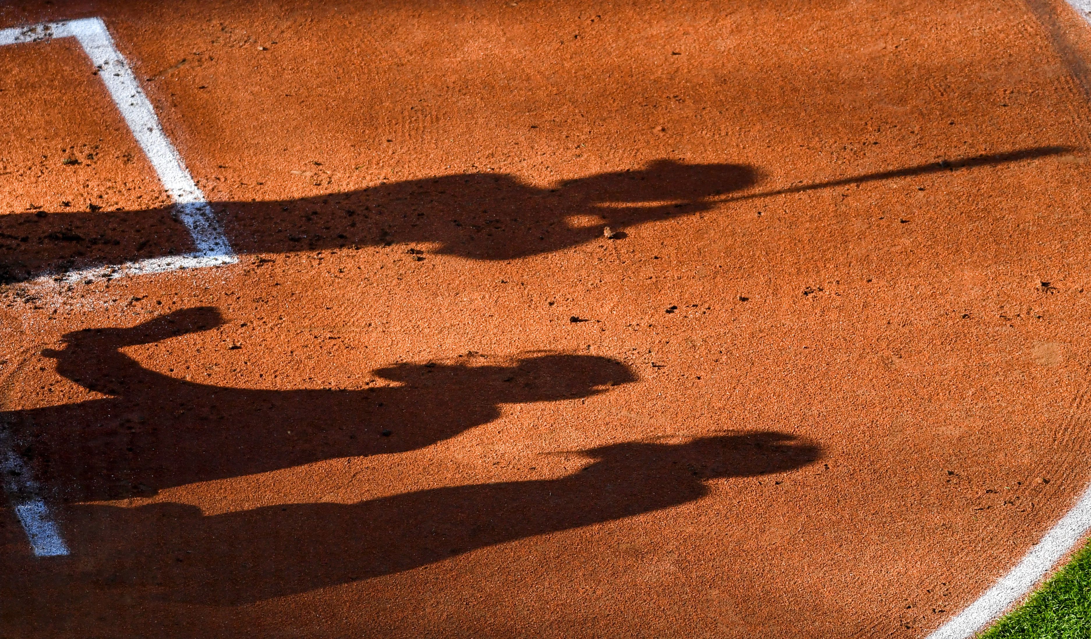 Shadows of a hitter, catcher, and umpire on a baseball field.