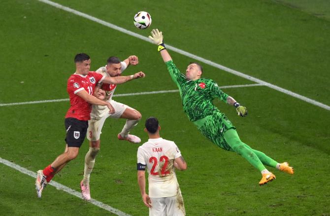 Mert Günok of Türkiye dives to make a save as Christoph Baumgartner of Austria competes for a header.