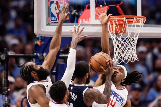 Dallas Mavericks Kyrie Irving goes up for a layup while being defended by LA Clippers James Harden, Paul George, and Terance Mann.