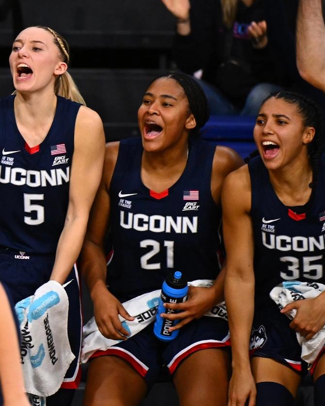 UConn basketball players Paige Bueckers, Sarah Strong, and Azzi Fudd celebrate on the bench during a game.