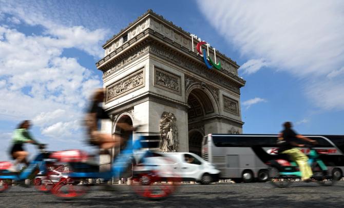 The Paralympic Agitos are seen on the Arc de Triomphe as blurred cars and people on bikes maneuver around the roundabout.