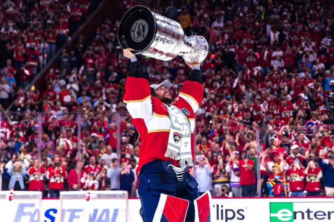 Florida Panthers goalie Sergei Bobrovsky raises the Stanley Cup above his head while the crowd cheers in the background.