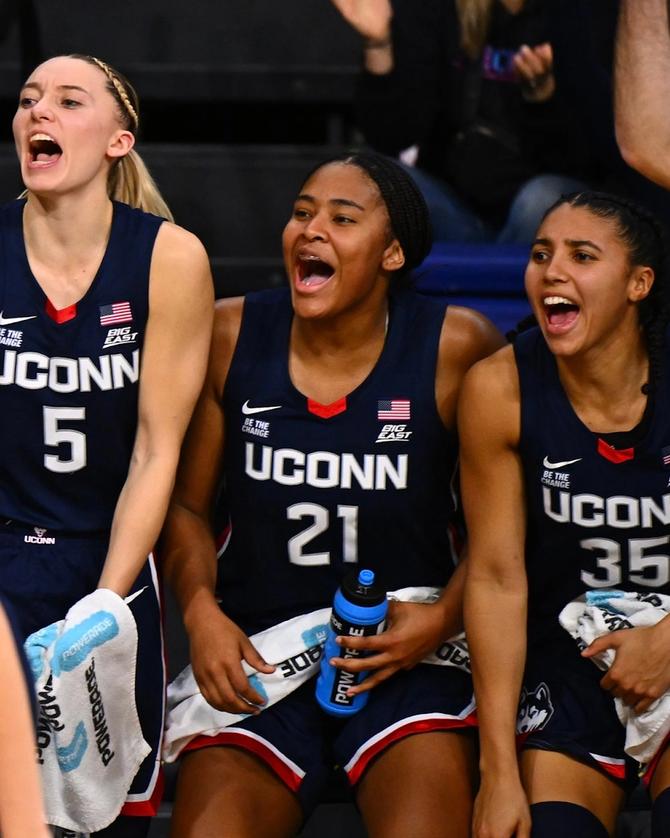 UConn basketball players Paige Bueckers, Sarah Strong, and Azzi Fudd celebrate on the bench during a game.