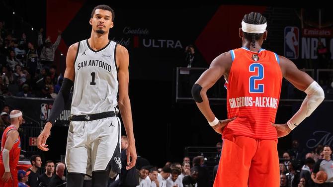 San Antonio Spur Victor Wembanyama looks at OKC Thunder star Shai Gilgeous-Alexander as he walks by him on the court.