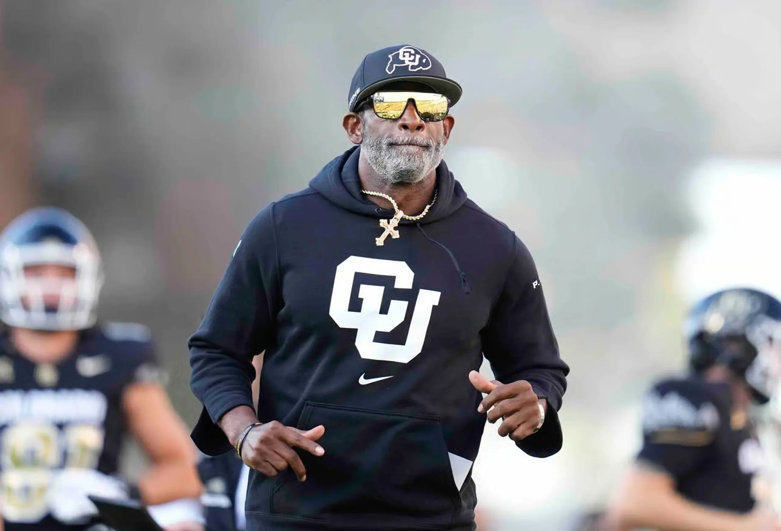 Deion Sanders jogs onto the field surrounded by his players.
