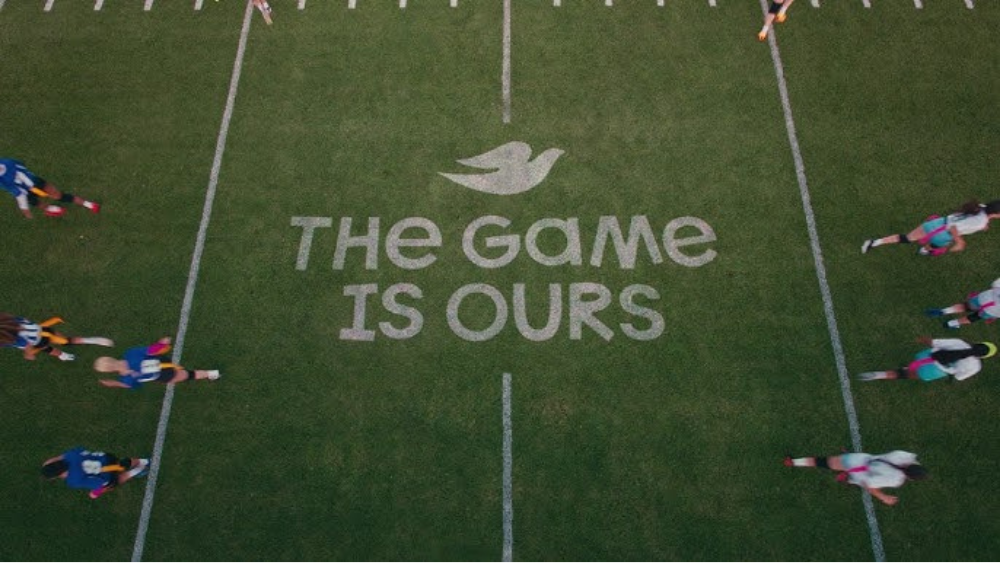 Aerial view of a sports field with athletes running along both sidelines and the words "The Game Is Ours" painted at the center.