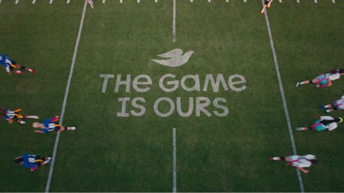 Aerial view of a sports field with athletes running along both sidelines and the words "The Game Is Ours" painted at the center.