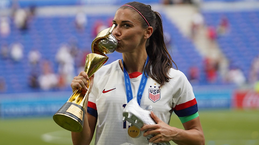 Former USWNT forward Alex Morgan kisses the Women's World Cup trophy.