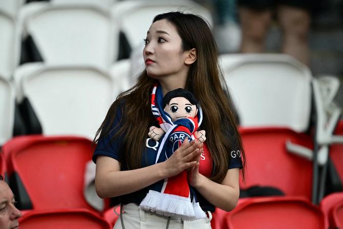 A woman with a supporter scarf holds a puppet of Paris Saint-Germain's South Korean midfielder #19 Lee Kang-in before the French L1 football match between Paris Saint-Germain (PSG) and Toulouse (TFC) on May 12, 2024 at the Parc des Princes stadium in Paris.