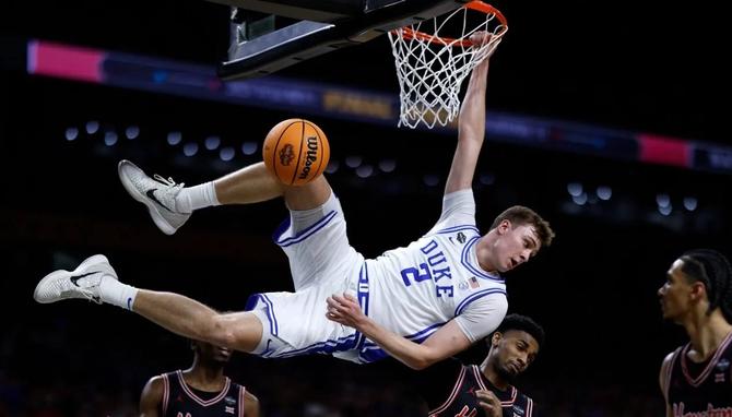 Duke’s Cooper Flagg hangs sideways off the rim after dunking the ball.