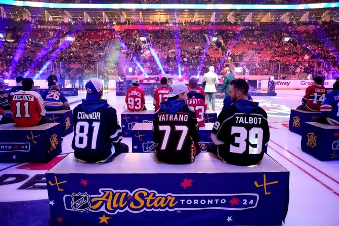 2024 NHL All-Stars sit together on benches set up on the ice waiting to be drafted.