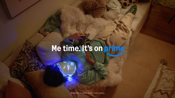 A woman in her living room opens an Amazon box containing an LED face mask, text reads "Me Time. Same Day Delivery. It's on Prime"
