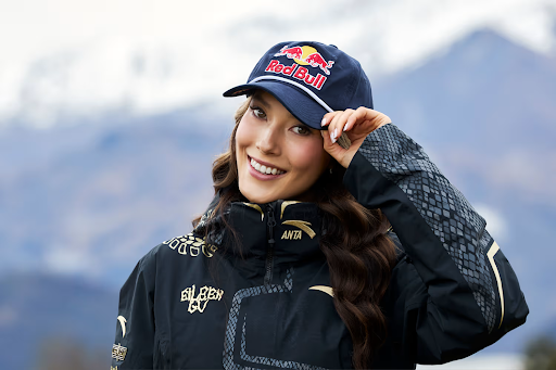 Eileen Gu poses in a Red Bull ball cap in front of a mountain landscape.