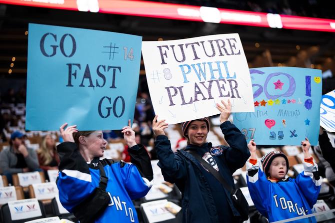 Young fans holding up signs at a PWHL game