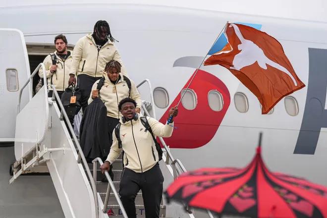 Members of the Texas football team step off a plane, waving a Longhorns flag.