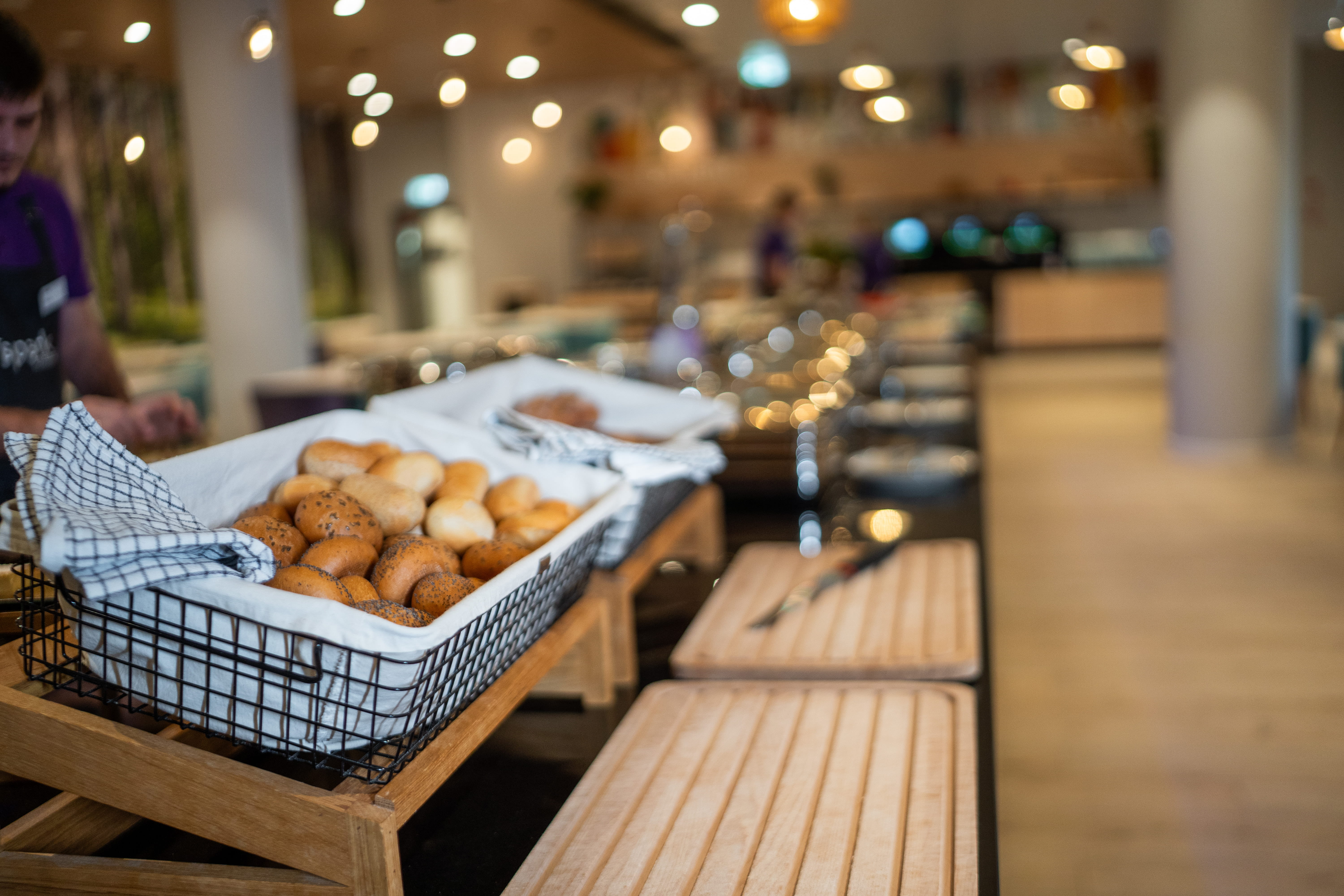 Restaurant buffet with baskets of assorted bread and pastries on a wooden table.