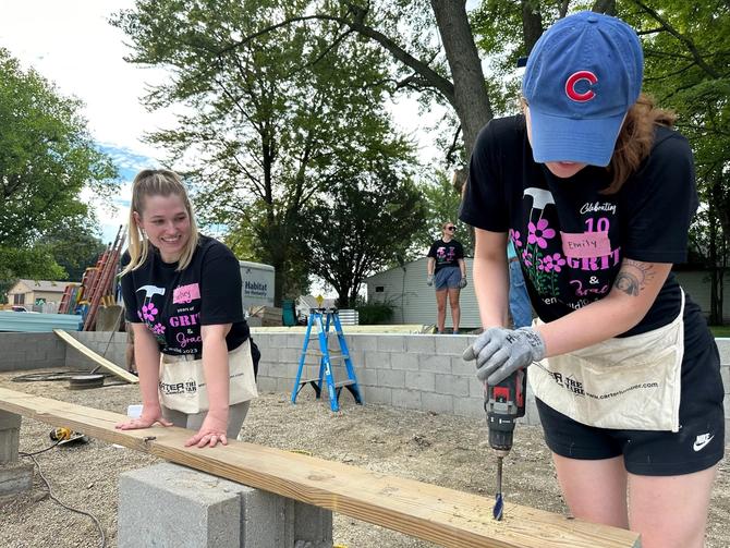 Two girls working on a plank of wood outside