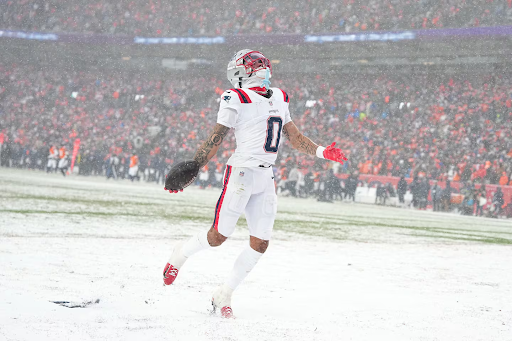 New England Patriots cornerback Christian Gonzalez extends his arms as he holds a football in his outstretched hand.