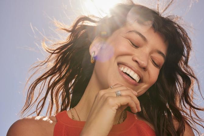 A woman smiling under the sun wearing jewellry