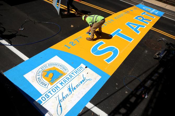 A worker spray paints details on the start line of the 127th Boston Marathon
