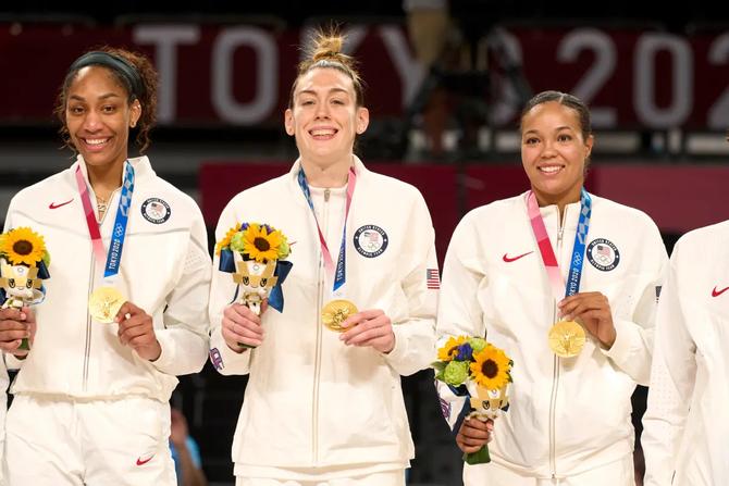WNBA and Team USA players A’ja Wilson, Breanna Stewart, and Napheesa Collier pose atop the Olympic podium with their gold medals at the 2020 Tokyo Games.