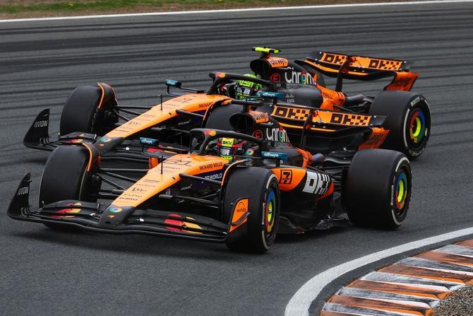The McLaren cars of Lando Norris and Oscar Piastri maneuver around a corner on track.