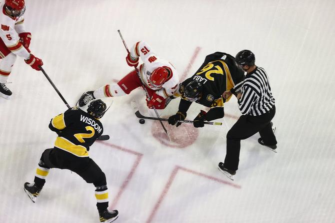 A referee drops a puck during a face-off between Denver and Colorado College men’s hockey players.