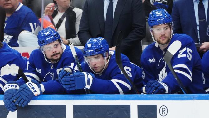 Toronto Maple Leafs Auston Matthews, Mitch Marner, and Brandon Carlo sit on the bench looking unimpressed.