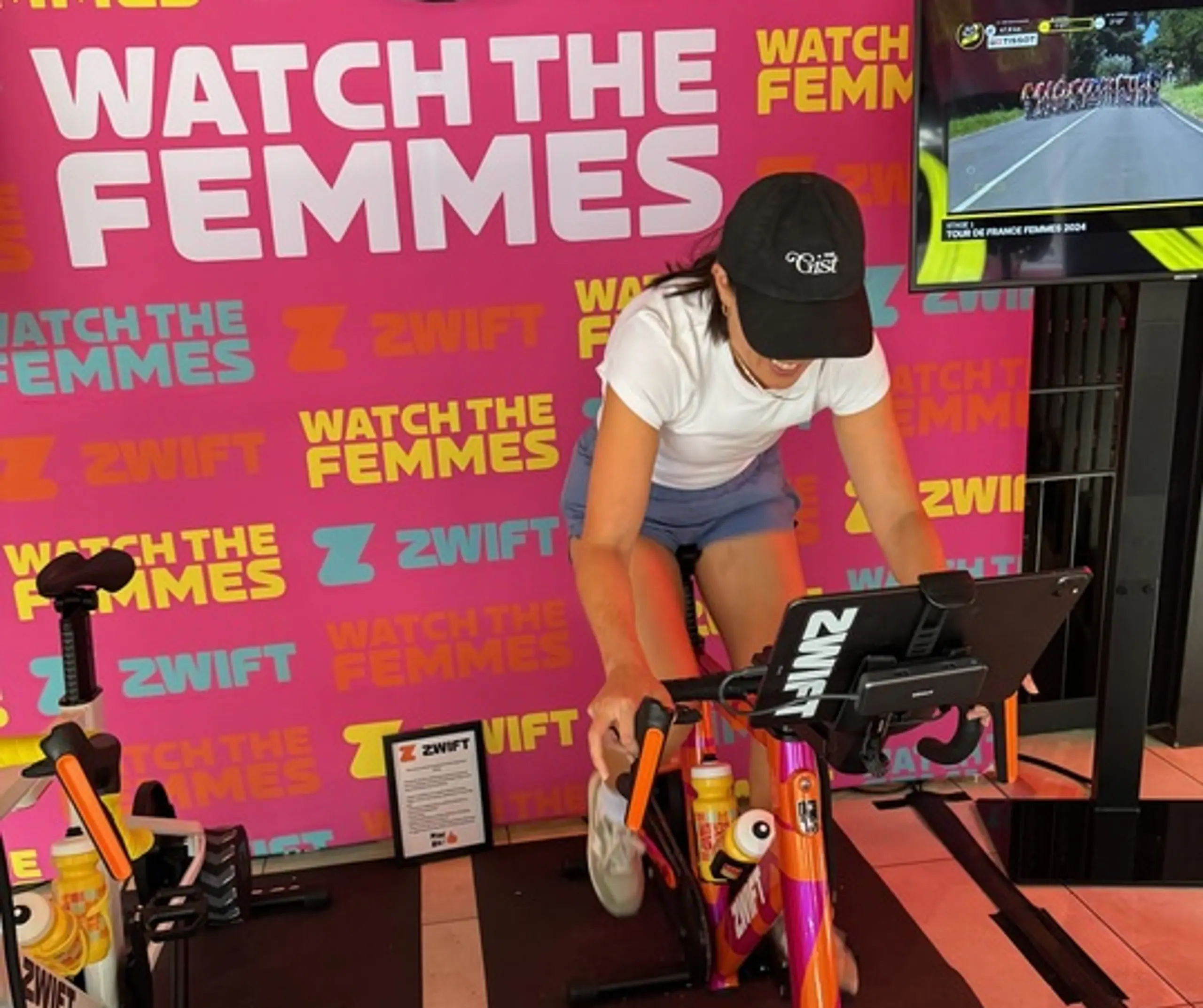 Jacie deHoop rides a Zwift indoor cycle at the 2024 Tour de France Femmes in her GIST cap.
