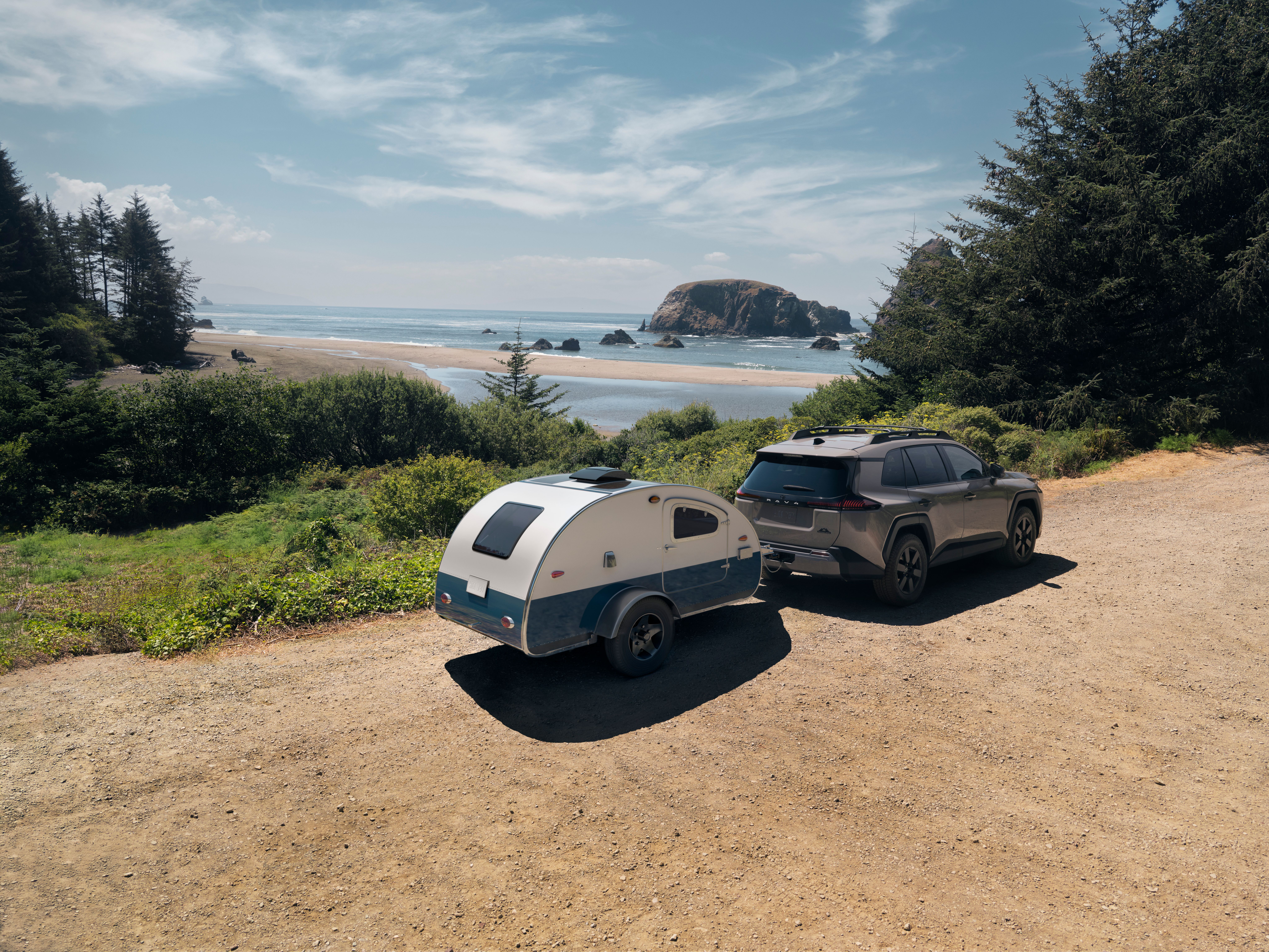 A RAV4 is on a dirt road, driving to the beach while towing a trailer