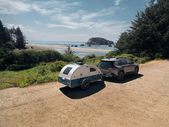 A RAV4 is on a dirt road, driving to the beach while towing a trailer