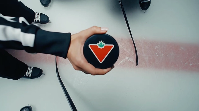 A Canadian tire logo is pictured on a hockey puck that is being held by an official.