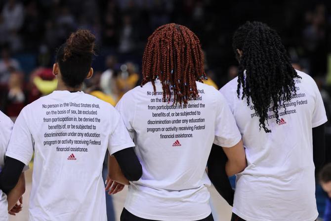 Players join arms wearing shirts with the Title IX language