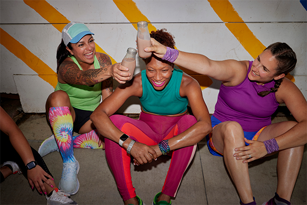 A group of women sitting on the ground, smiling and clinking bottles