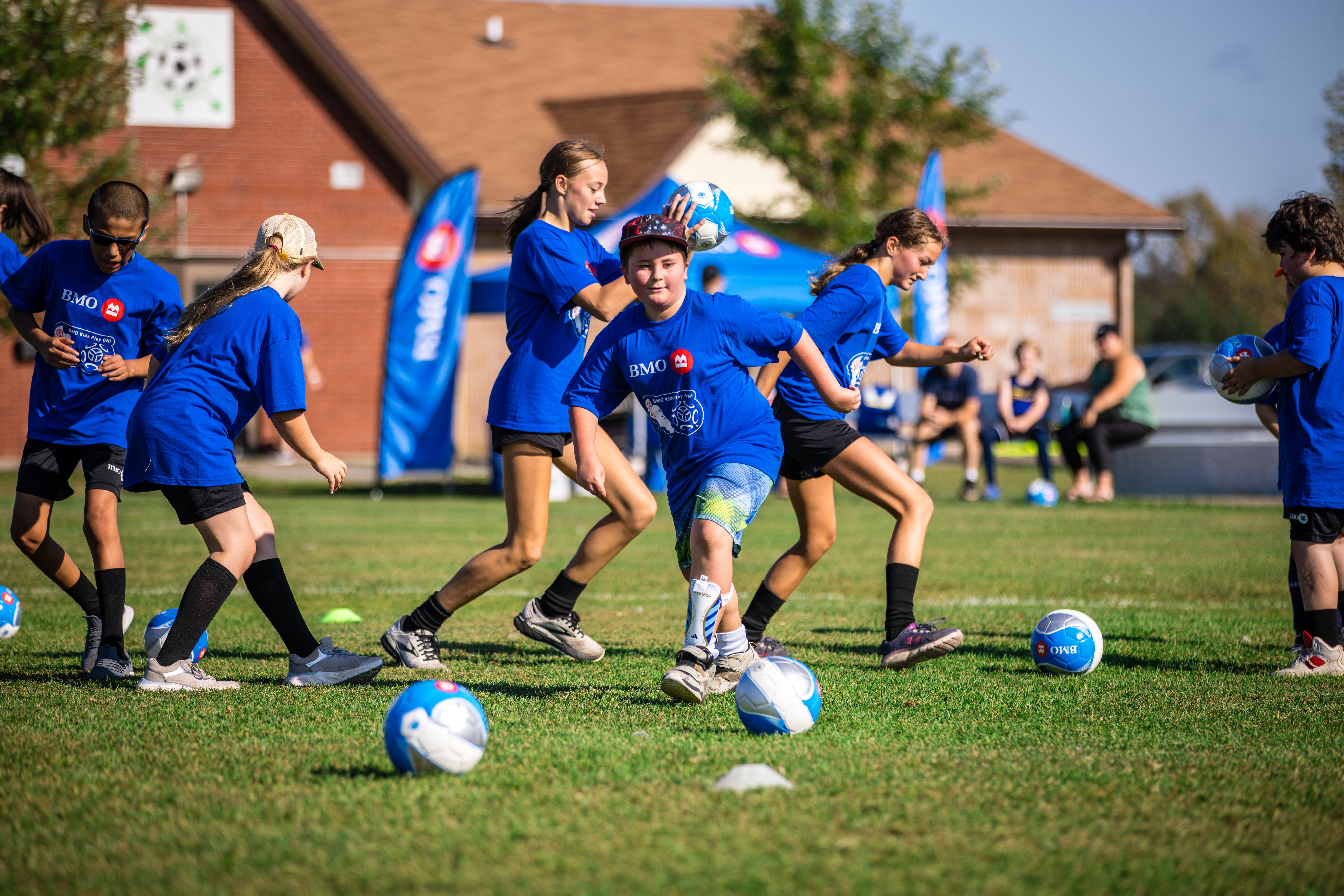 Kids playing on a soccer field wearing blue BMO jerseys