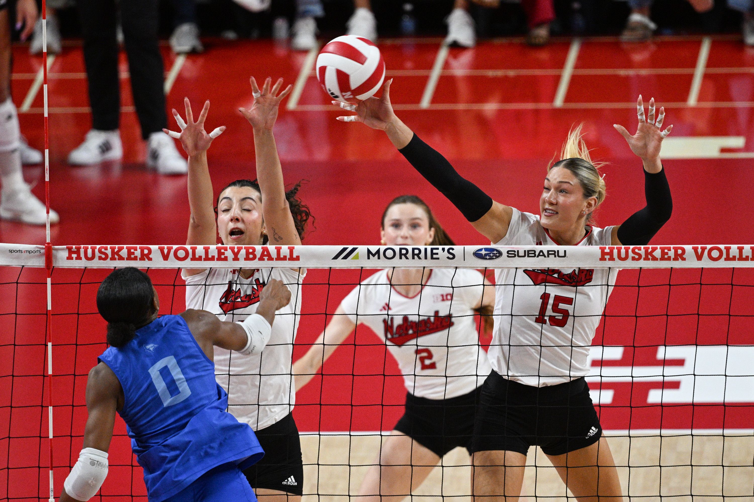 Virginia Adriano and Andi Jackson of the Nebraska Cornhuskers attempt a block against Trinity Shadd-Ceres of the Creighton Bluejays.