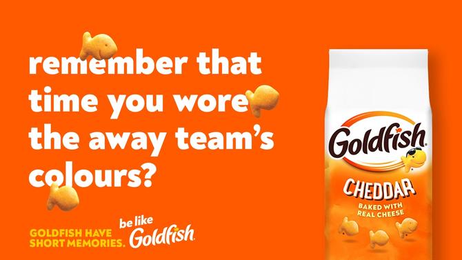 Goldfish ad with the text: 'Remember that time you wore the away team’s colours?' and a bag of Cheddar Goldfish crackers on an orange background.