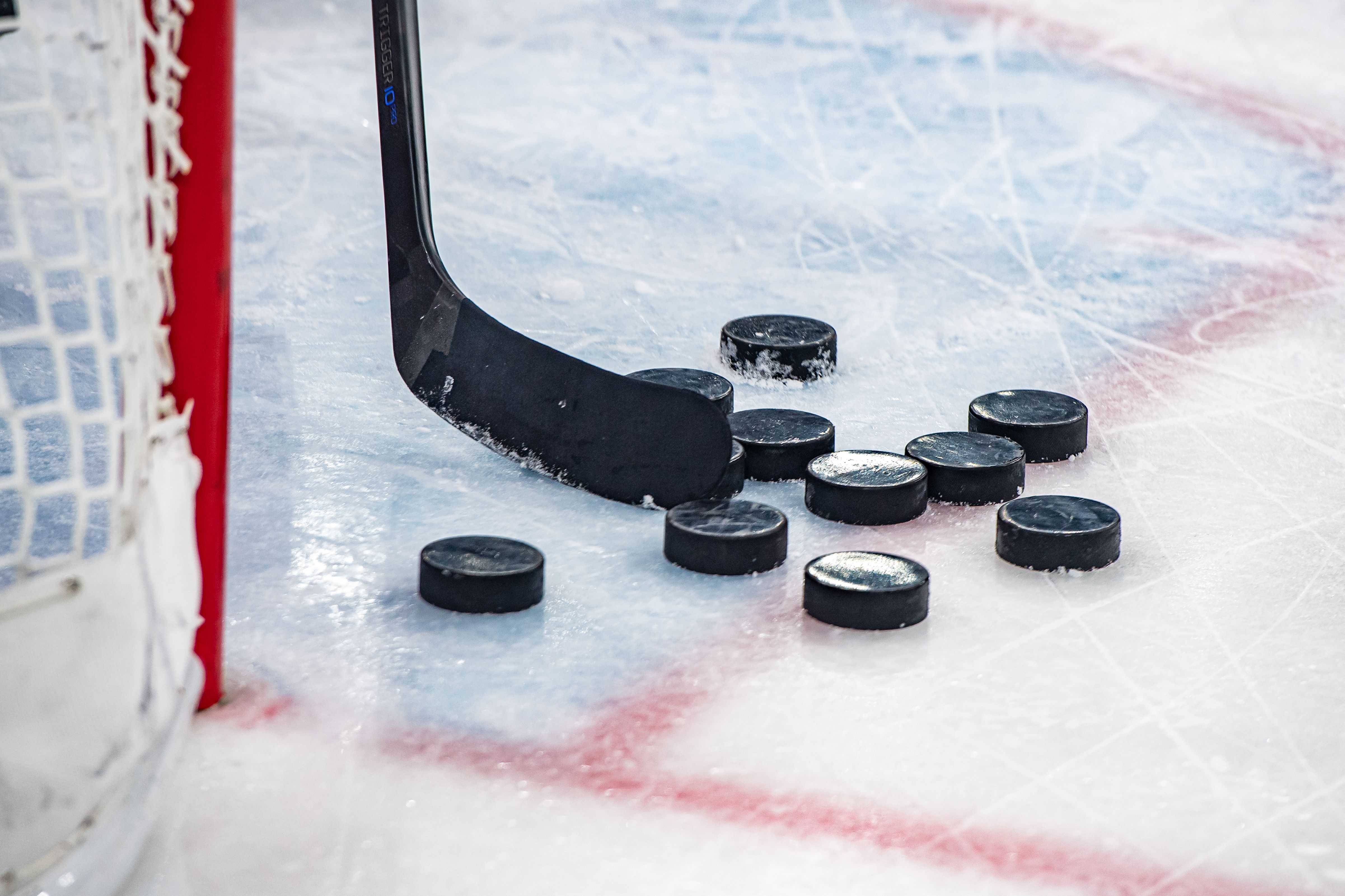 Ice hockey stick next to a net with pucks scattered around.