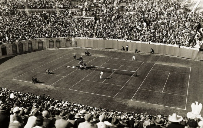A black and white photo depicting three tennis courts surrounded by stands at one of the original US Open events.