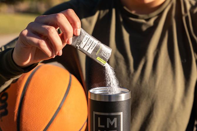 A person pouring an LMNT pouch into an LMNT cup while holding a basketball