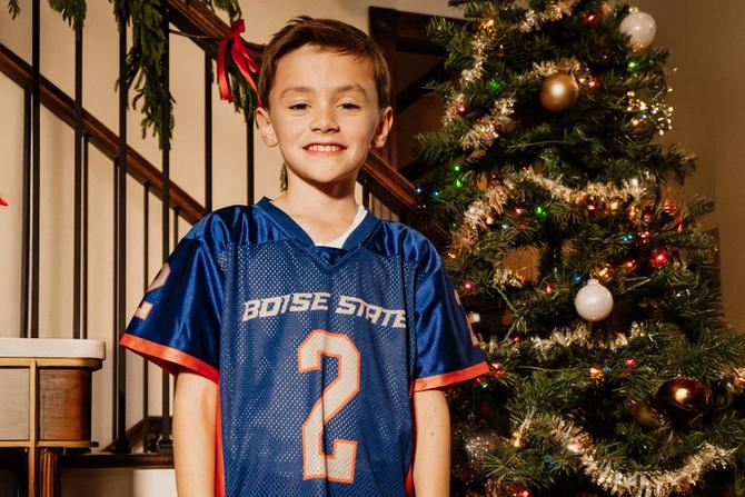 A little boy smiling while wearing a Boise State jersey