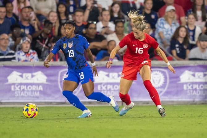 USWNT defender Crystal Dunn turns away from CanWNT forward Janine Beckie during a soccer match.