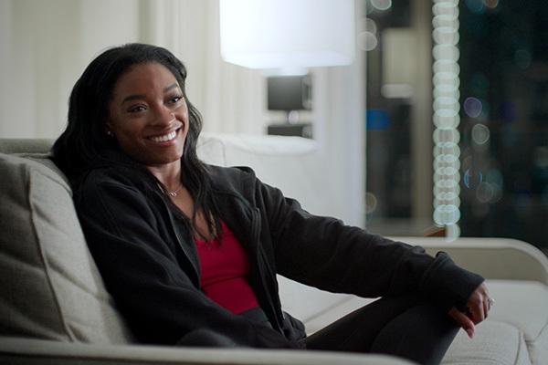 Simone Biles smiling from a couch